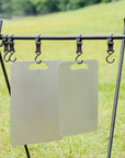 Two Keith Titanium titanium cutting boards hanging from hooks on an outdoor camp rack