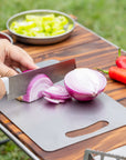 Close-up of a red onion being sliced on a Keith Titanium titanium cutting board outdoors
