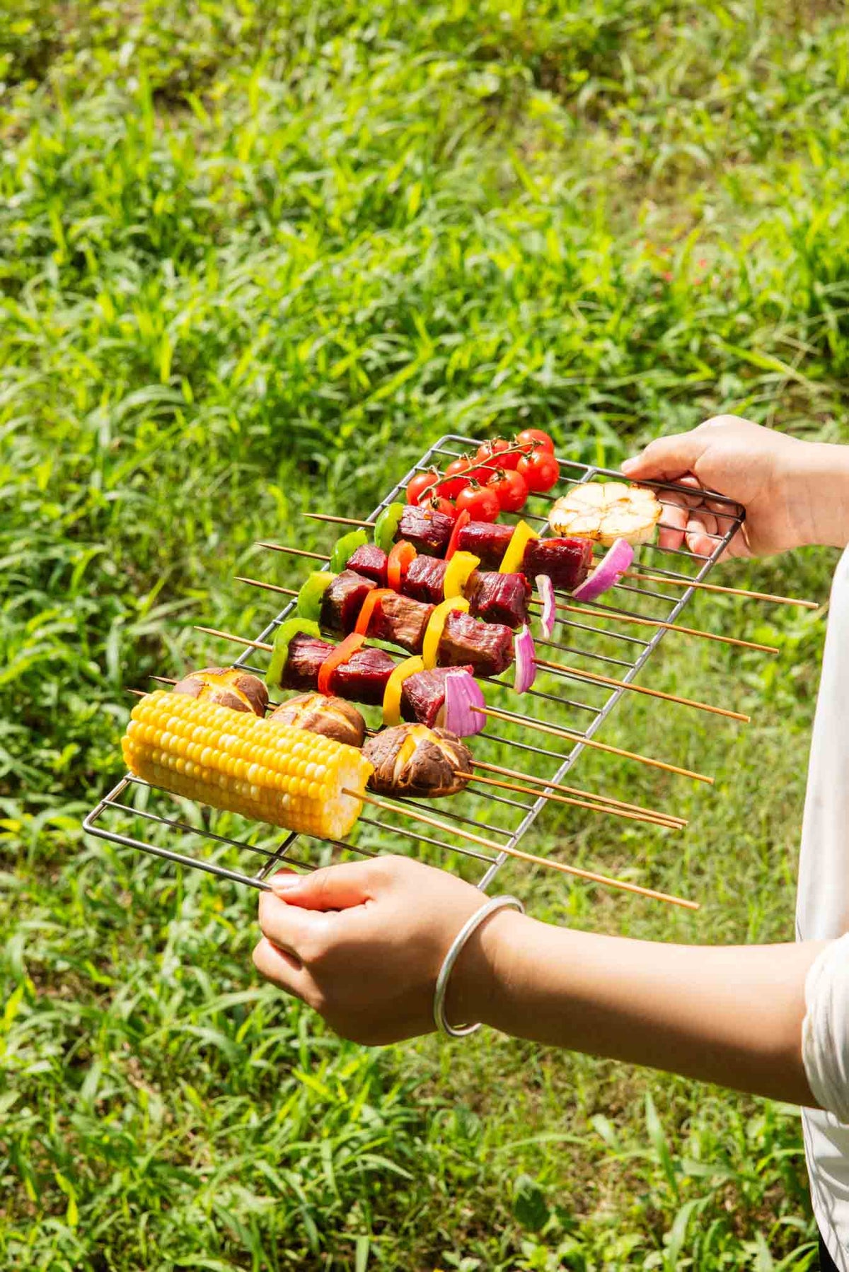 Hands carrying the Keith Titanium Ti2211 grill mesh loaded with skewers and vegetables