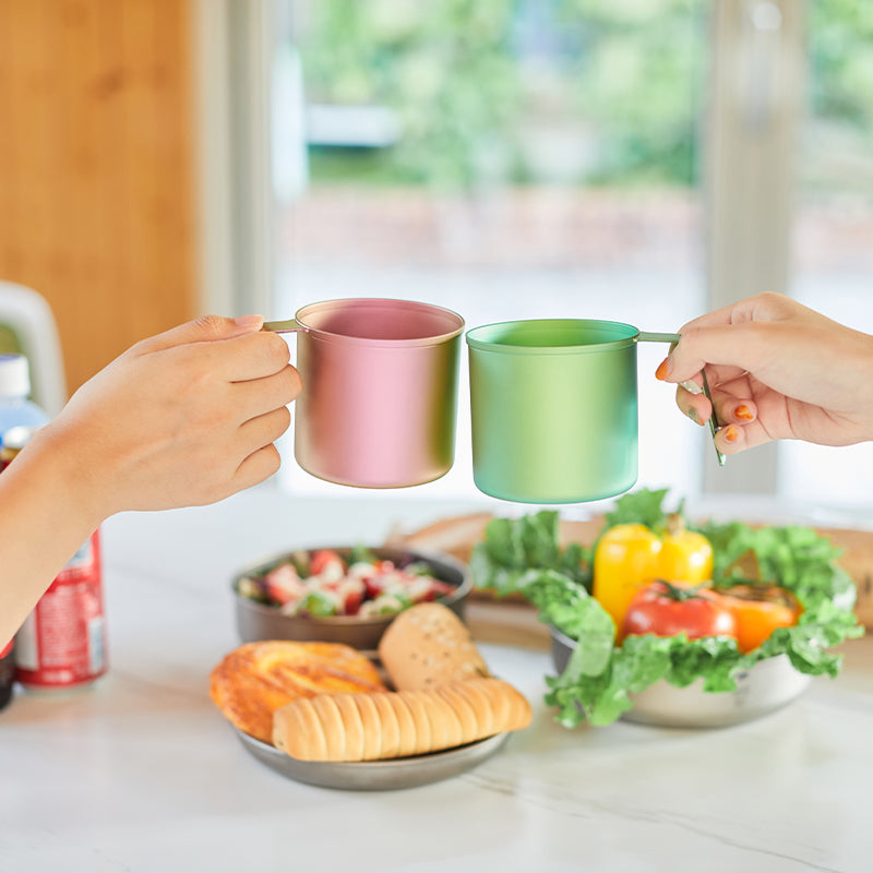 Two hands toasting Keith Titanium pink and green radiant spectrum cups over a table of food