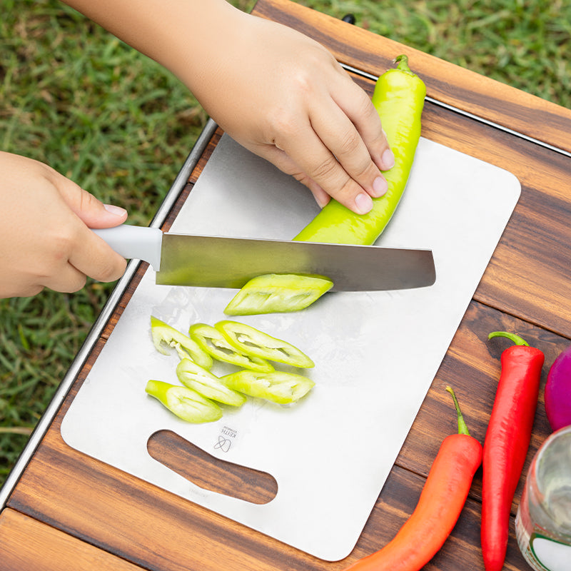 Keith Titanium titanium cutting board being used to slice a green pepper on an outdoor table