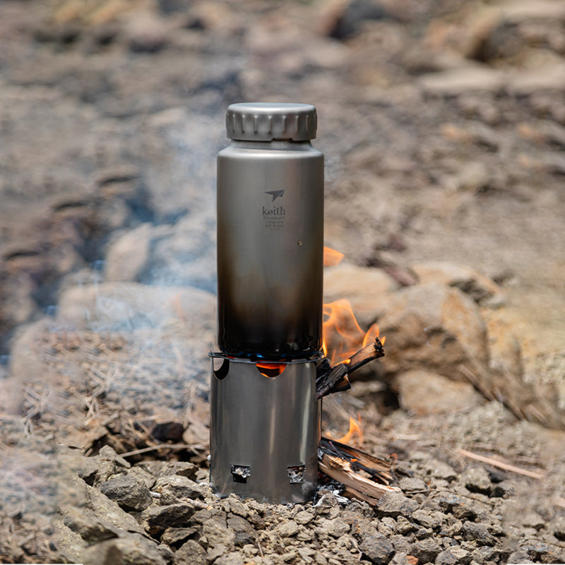 Keith Titanium Ti3070 bottle heating on a wood stove over an open campfire