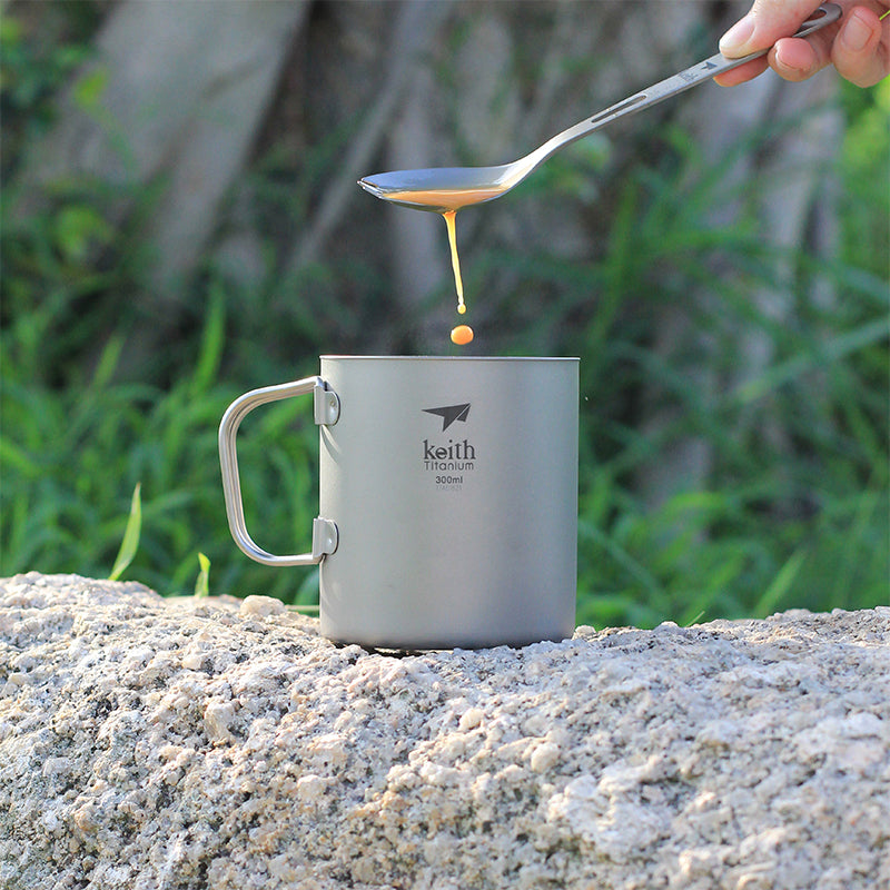 Keith Titanium Ti3353 mug with honey dripping from a spoon into the cup on a rock outdoors
