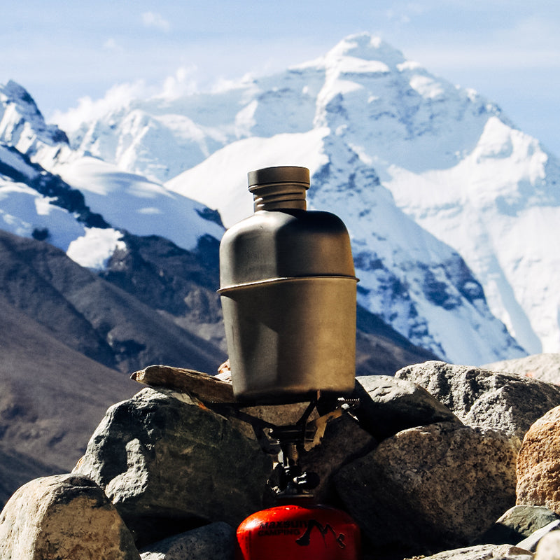 Keith Titanium Ti3060 canteen mess kit heating on a backpacking stove in front of snow-covered mountains