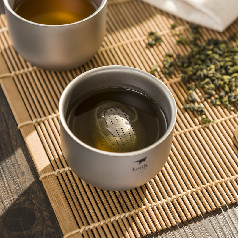 Keith Titanium Ti3906 tea cup holding tea with a tea infuser on a bamboo mat
