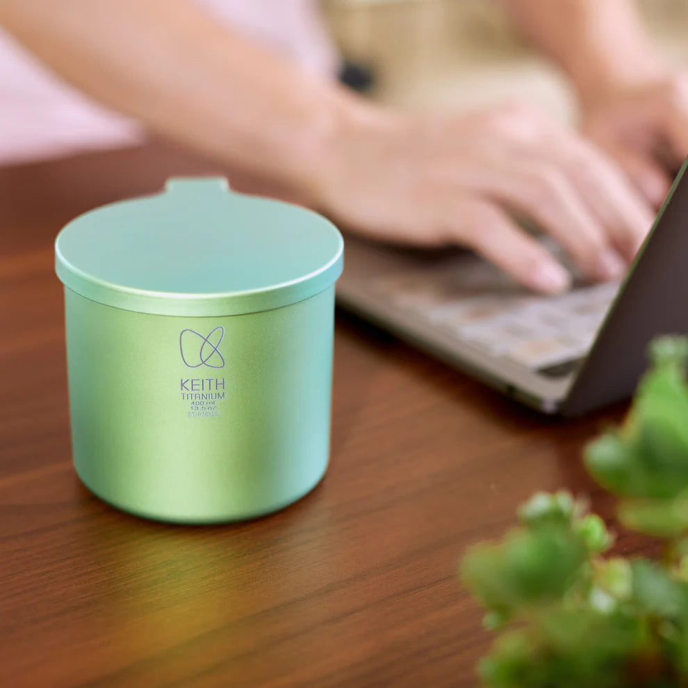 ノートパソコンの横の木製テーブルに置かれたKEITH Titaniumスプリンググリーンカラーカップ