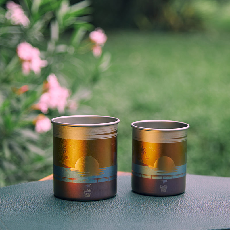 屋外テーブルに置かれた2個のKEITH Titanium Artisan Sunset Glowマグ