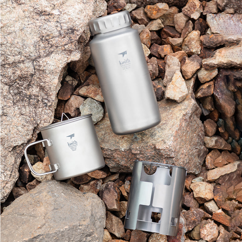 Keith Titanium Ti3070 bottle, mug, and wood stove sleeve arranged on rocky ground