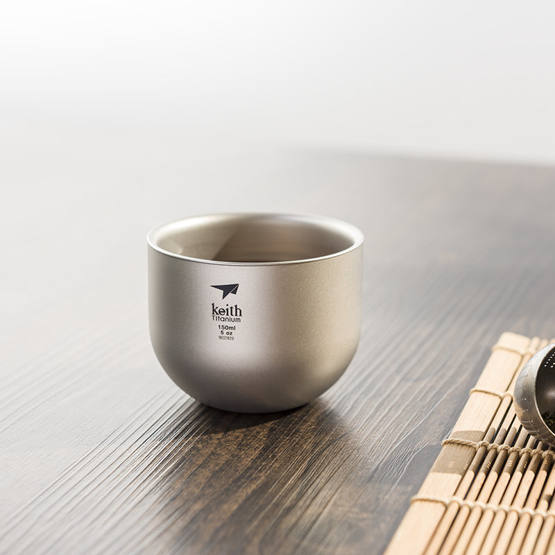 Keith Titanium Ti3906 tea cup on a wooden table beside a bamboo mat and tea infuser