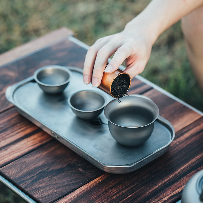 Loose tea being poured from a tin canister into a cup beside the Keith Titanium Ti3910 tea set