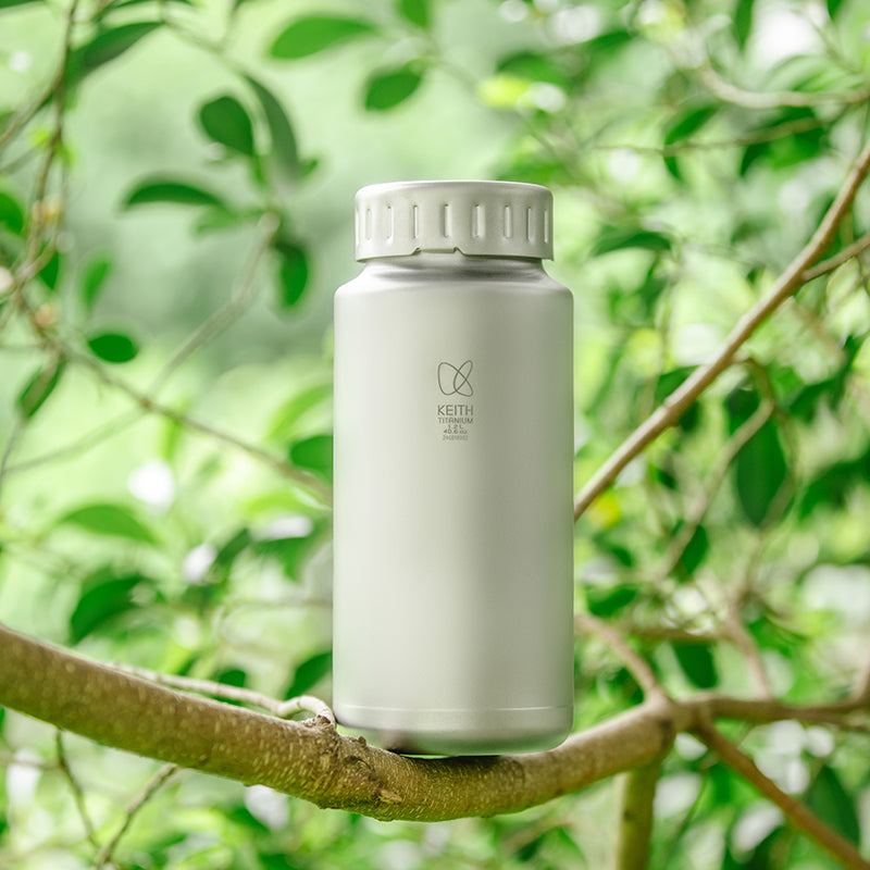 Keith Titanium Ti3036 titanium bottle standing on a tree branch with green leaves in the background
