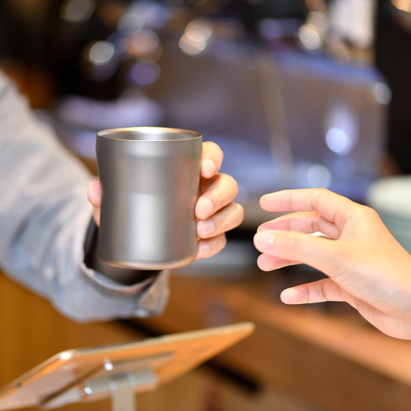 Hand holding the Keith Titanium Ti3312 mug across a cafe counter