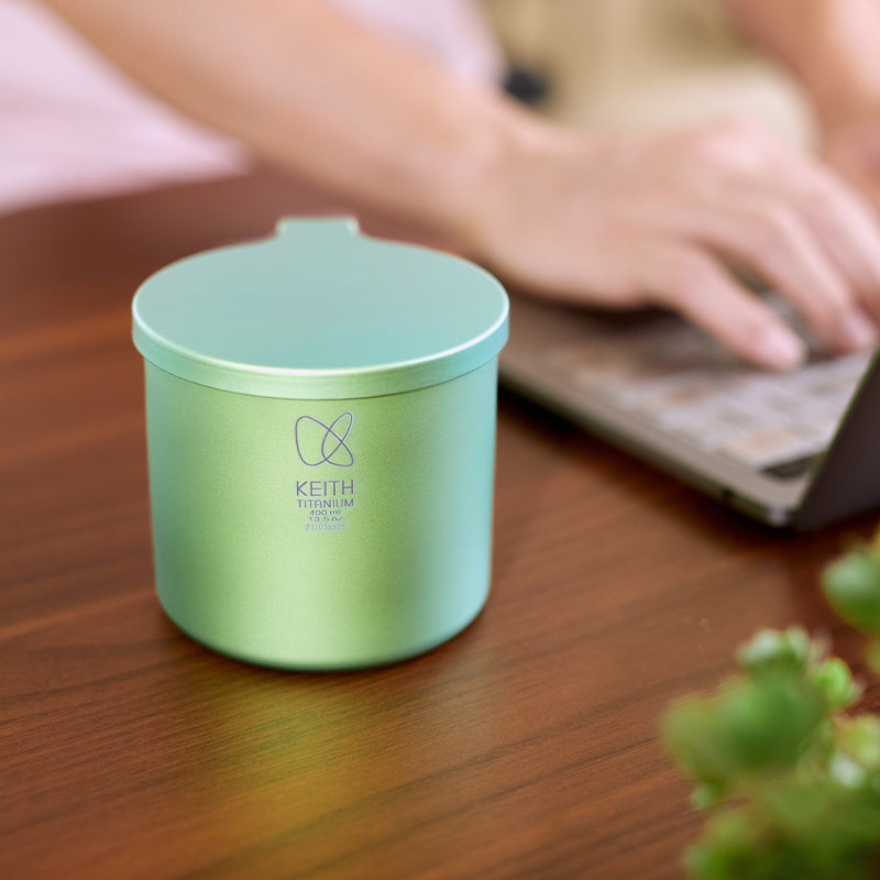 Keith Titanium spring green radiant spectrum cup on a wooden desk beside a laptop