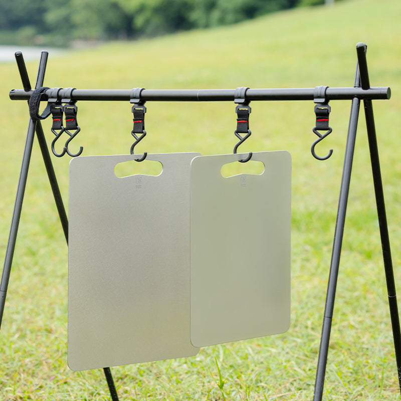 Two Keith Titanium titanium cutting boards hanging from hooks on an outdoor camp rack