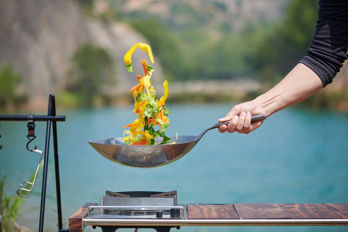 Hand tossing vegetables in the Keith Titanium forged titanium wok beside a lake
