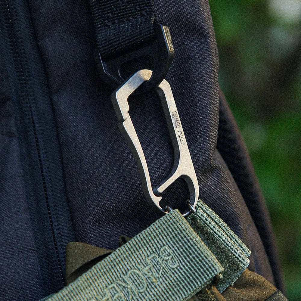 Keith Titanium Ti1155 carabiner clipped between a backpack strap and a green pouch outdoors