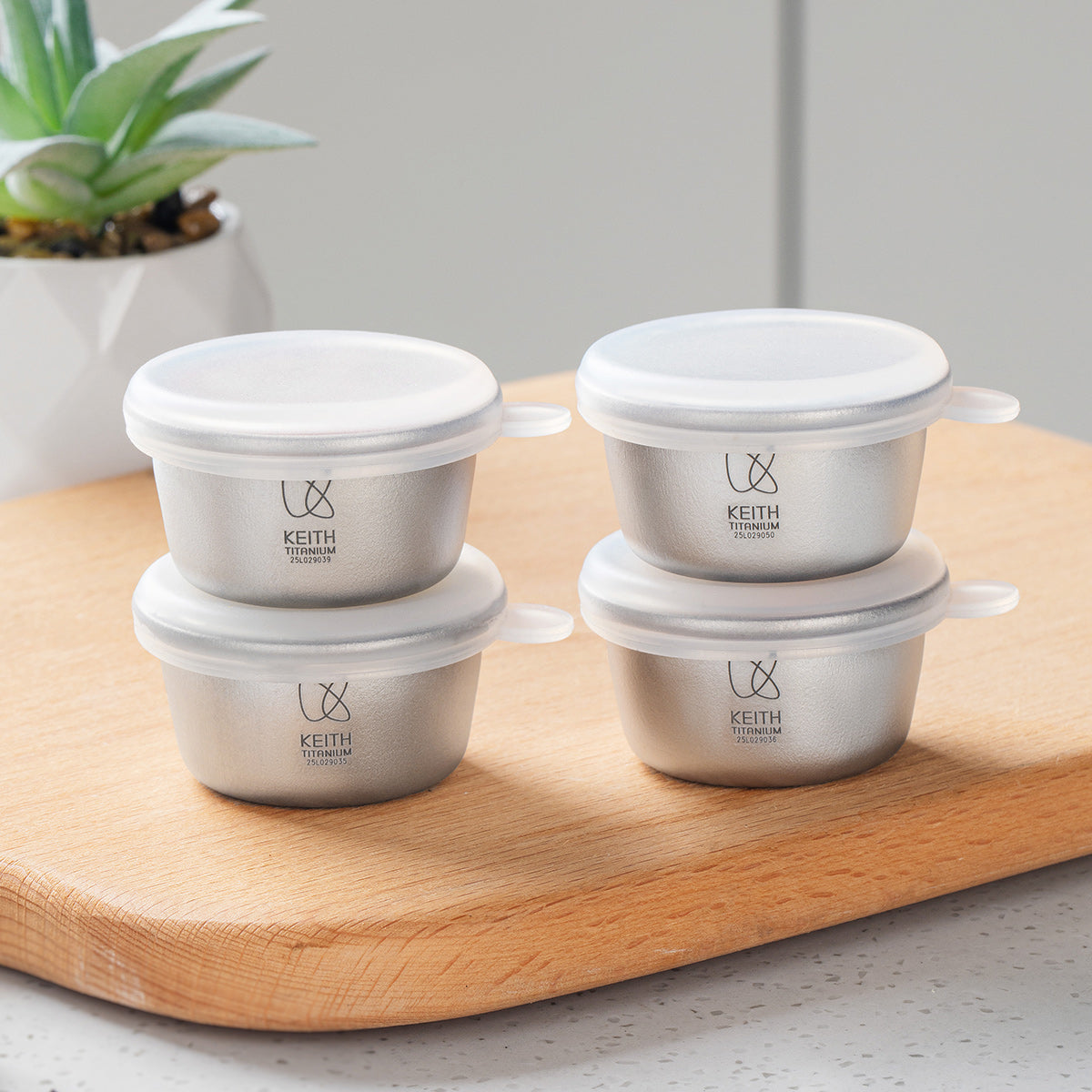 Four KEITH Ti1161 titanium mini containers with translucent silicone lids on a wooden board