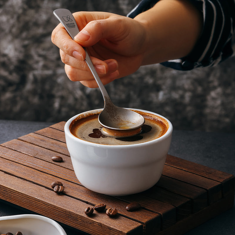 Hand using a Keith Titanium Ti3602 cupping spoon over a cup of coffee