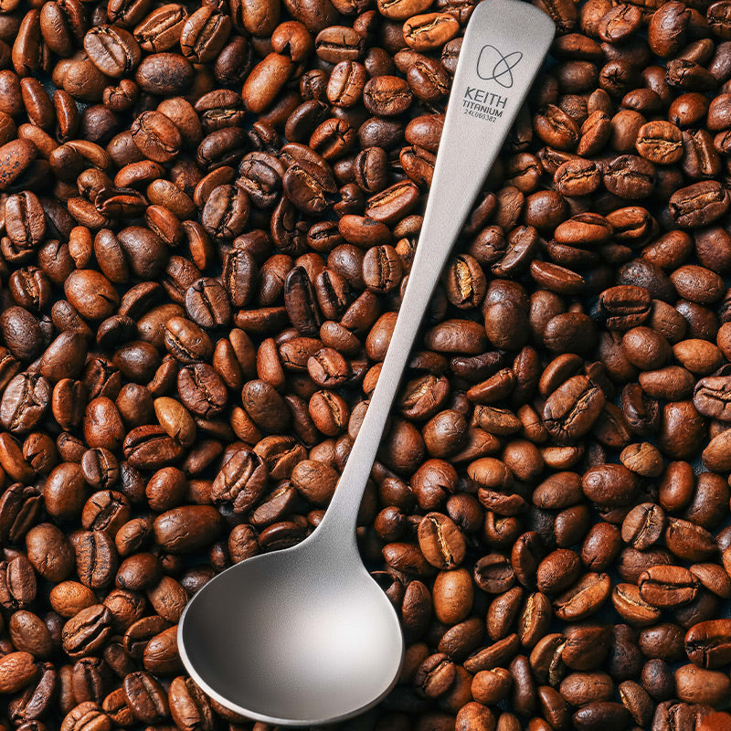 Keith Titanium Ti3602 coffee cupping spoon resting on roasted coffee beans