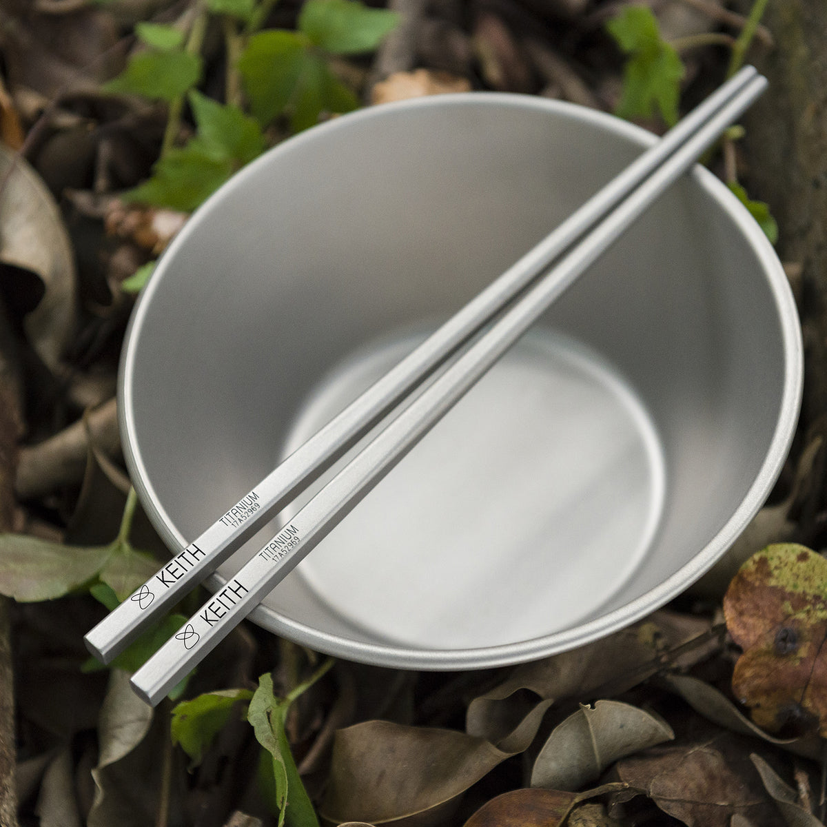 Keith Titanium Ti5633 titanium chopsticks resting across a titanium bowl outdoors