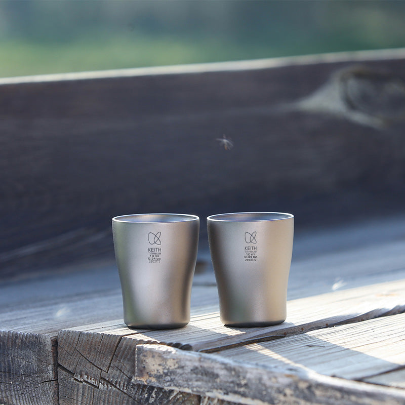 Two Keith Titanium Ti9304 shot glasses on a wooden bench outdoors