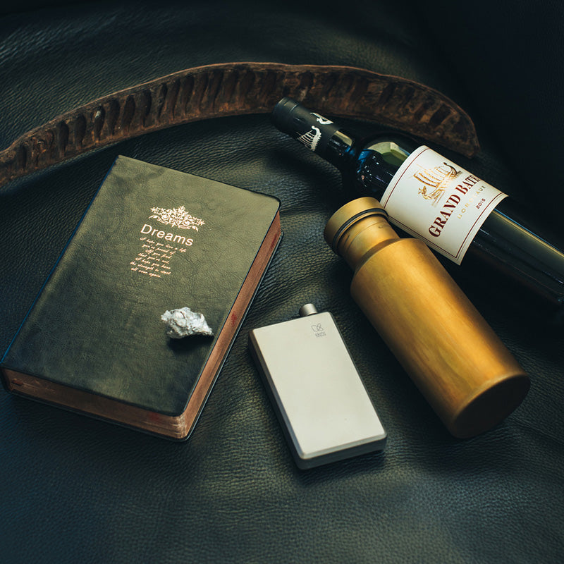 Keith Titanium Ti9306 pocket flask beside a bottle, book, and thermos on a dark surface