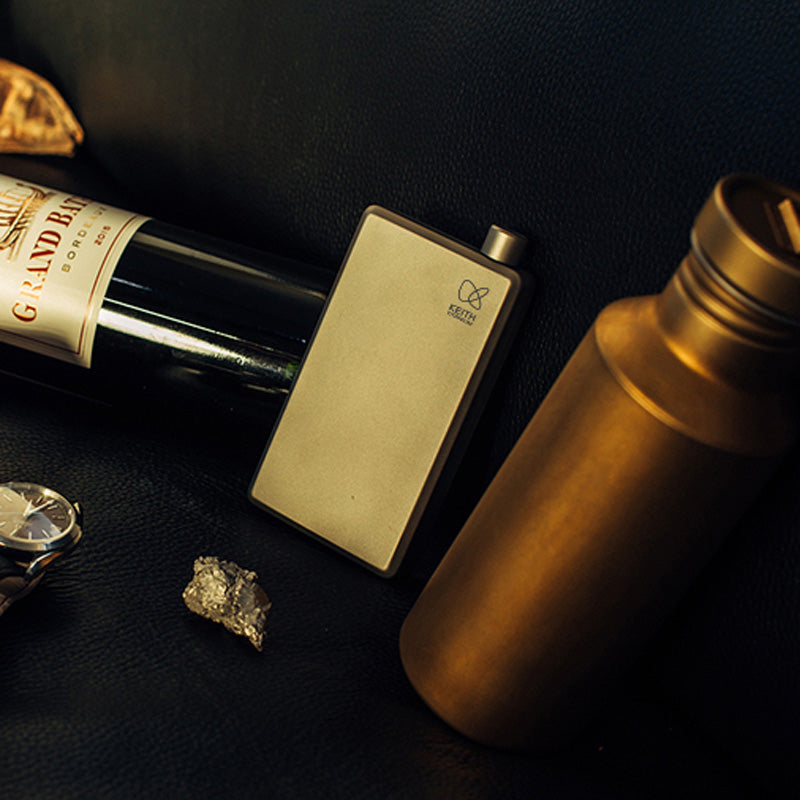 Keith Titanium Ti9306 pocket flask leaning against a bottle and thermos on a dark surface