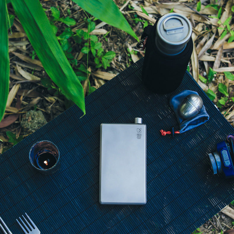 Keith Titanium titanium pocket flask on a black outdoor mat beside a cup and outdoor gear