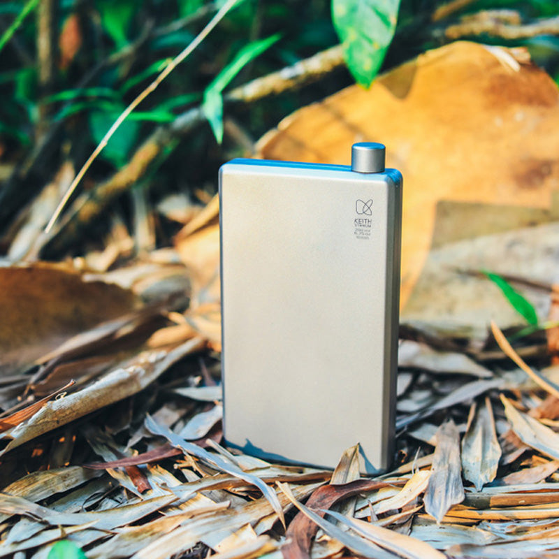 Keith Titanium titanium pocket flask standing among dry leaves outdoors